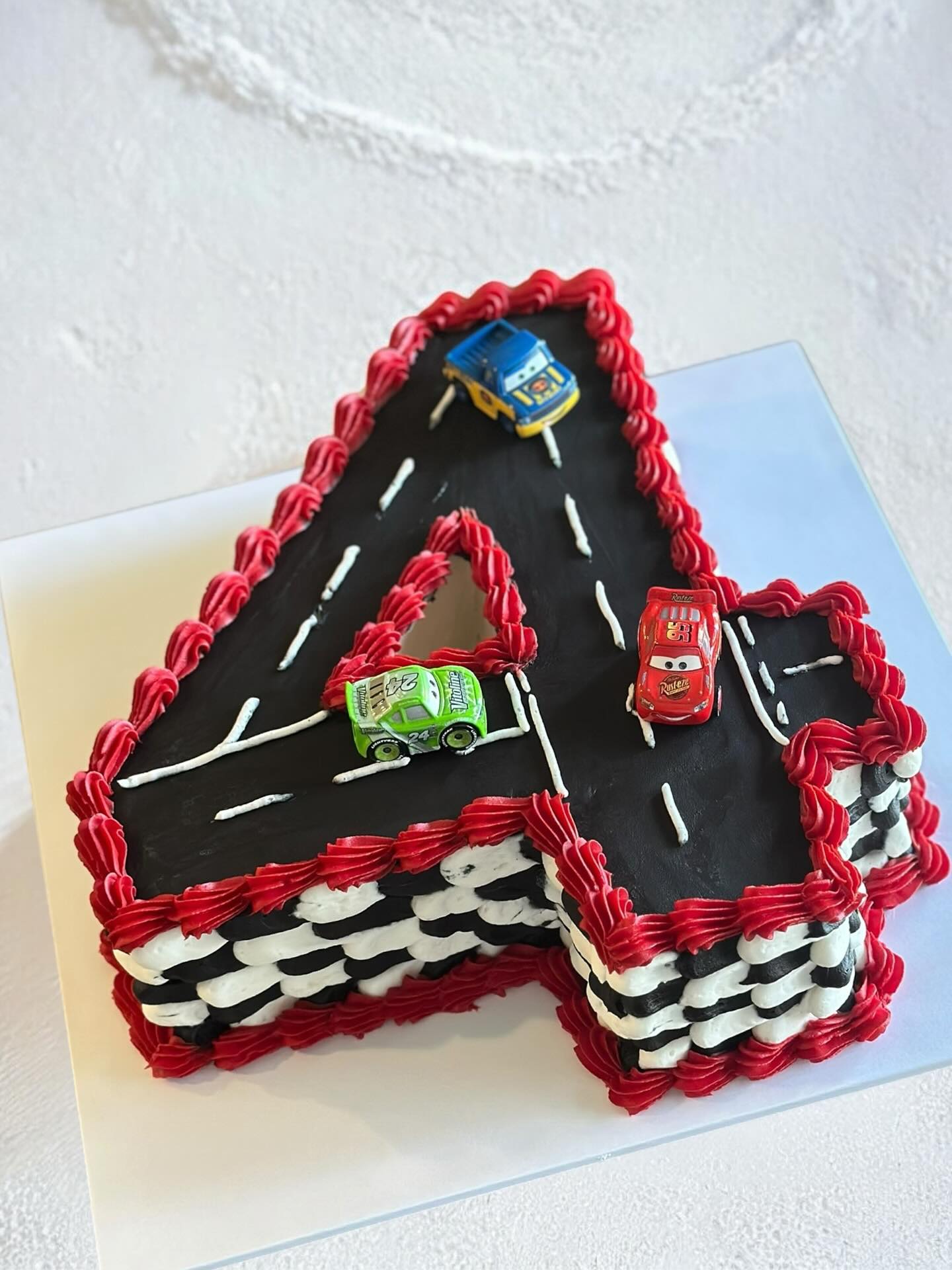 Cars-themed letter A birthday cake with red, black and white finishes